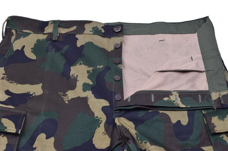 Close-up of genuine Hungarian M1990 military field pants in woodland camo with button fly and reinforced fabric.