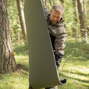 Man unrolling a compact lightweight gray British military sleeping pad in a forest setting