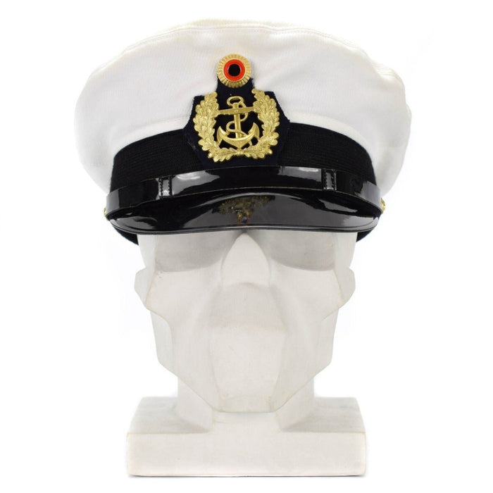 Berretto con visiera bianco da ufficiale della Marina tedesca con insegne dorate e visiera nera esposto su una testa di manichino bianco.