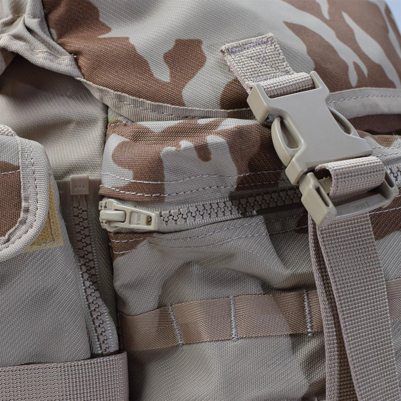 Close-up of desert camo military backpack showing zipper, buckle, and MOLLE strap detail.