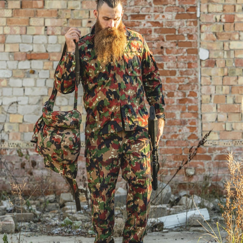 Man wearing Original Swiss Army M83 Alpenflage camo jacket and pants holding matching bag and walking in urban area