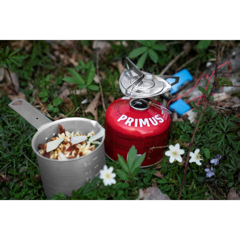 Primus Essential Trail KIT lightweight camping stove with 1L pot cooking outdoors surrounded by greenery and flowers