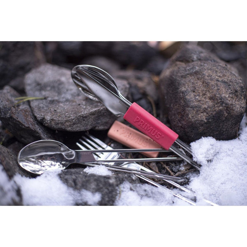Primus outdoor camping cutlery set with stainless steel knife, fork, spoon, and silicone handles on rocky snowy ground.