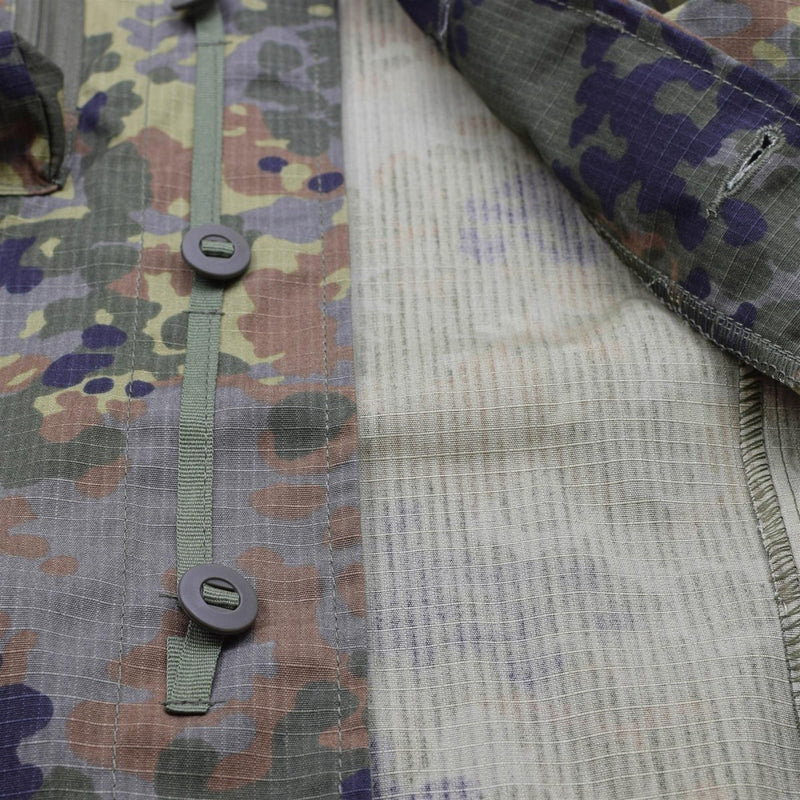 Close-up of TACGEAR Flecktarn camo jacket fabric showing buttons, ripstop texture, and military pattern details.